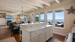 A spacious kitchen with a large island, white cabinetry, and a view of the ocean. - Seagrape 5 Bedroom Home (Port Bolivar)