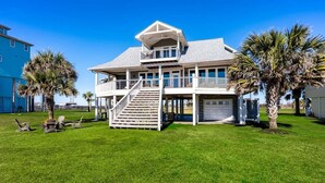 A two-story house with a balcony and a covered porch, surrounded by a well-maintained lawn and palm trees. - Seagrape 5 Bedroom Home (Port Bolivar)
