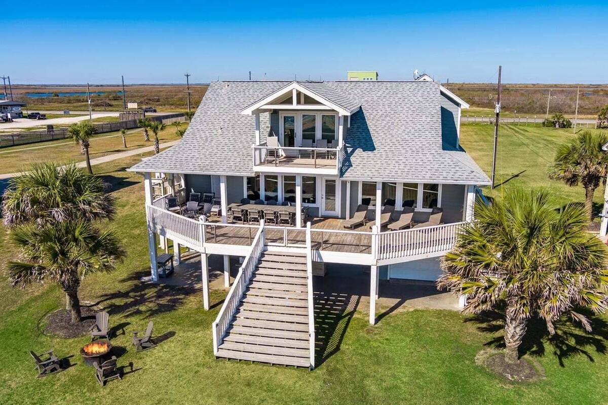 A two-story house with a covered porch and a deck, surrounded by palm trees and a clear sky.