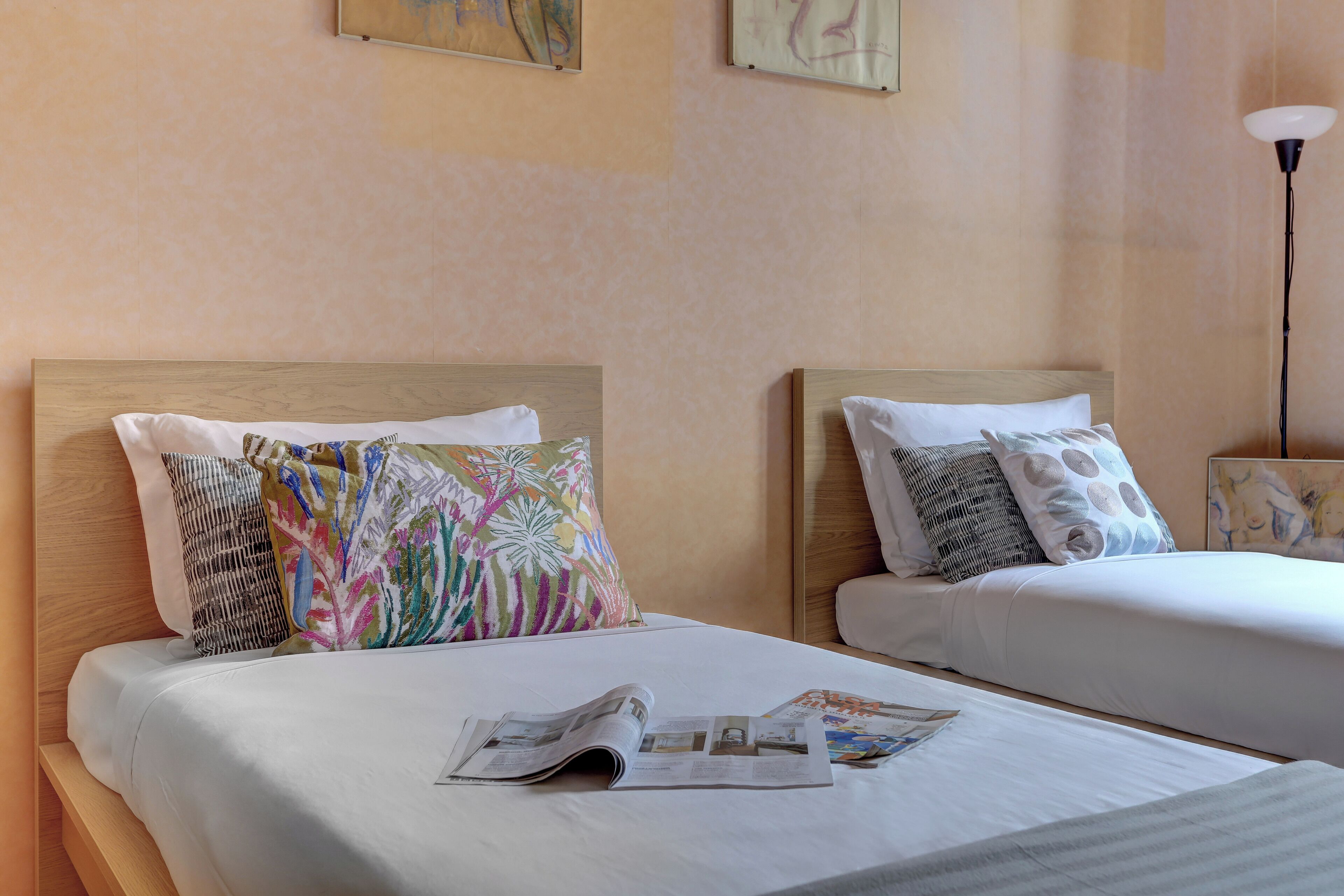 Dos camas individuales con sábanas blancas, almohadas coloridas y una revista sobre la cama.