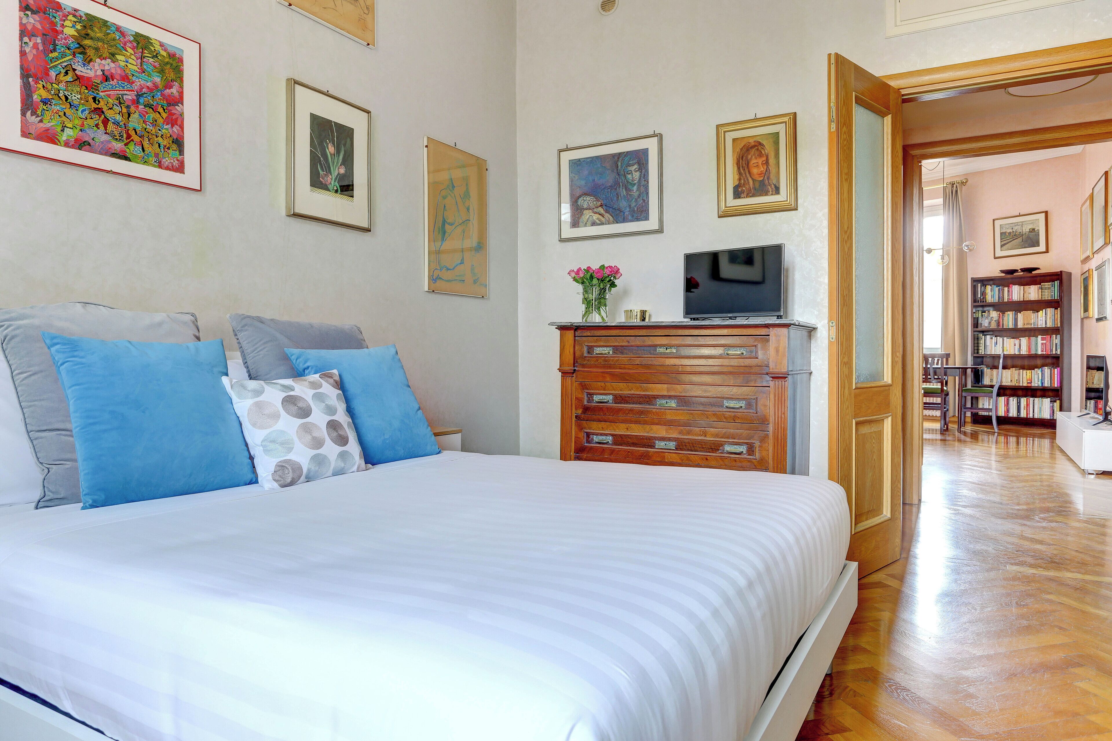 A bedroom with a large bed, a dresser, a television, and a bookshelf.