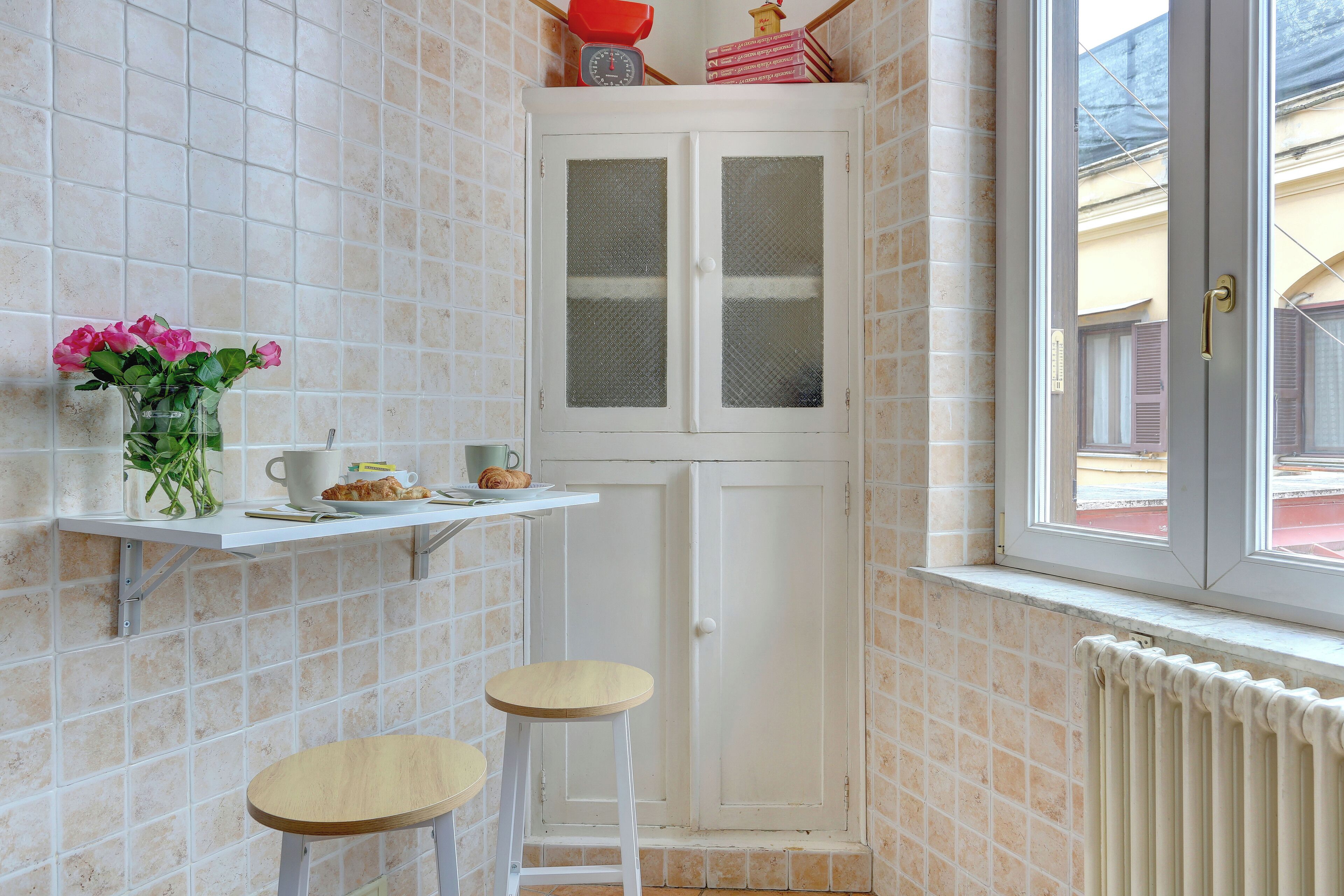 A small kitchen with a white cabinet, a window, and a shelf with a vase of flowers.