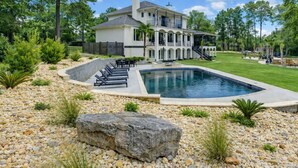 Une grande maison avec une piscine, entourée d’un jardin aménagé avec des rochers et des plantes.