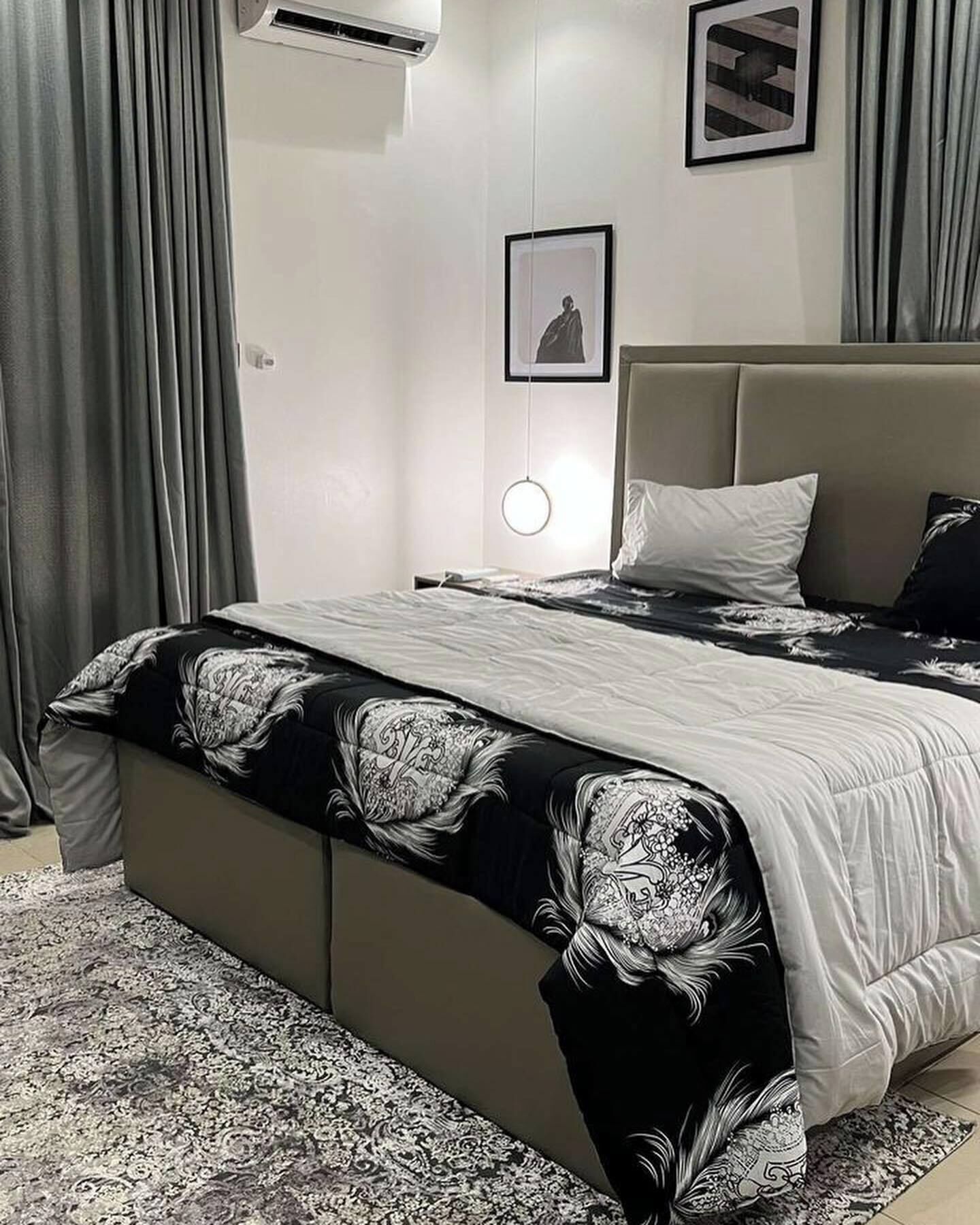 A modern bedroom with a large bed, grey curtains, a wall-mounted air conditioner, and a framed picture.