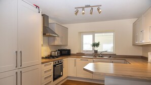 Een moderne keuken met witte kasten, een roestvrijstalen afzuigkap, een magnetron, een broodrooster en een spoelbak. Er is een raam met een plant op de vensterbank.