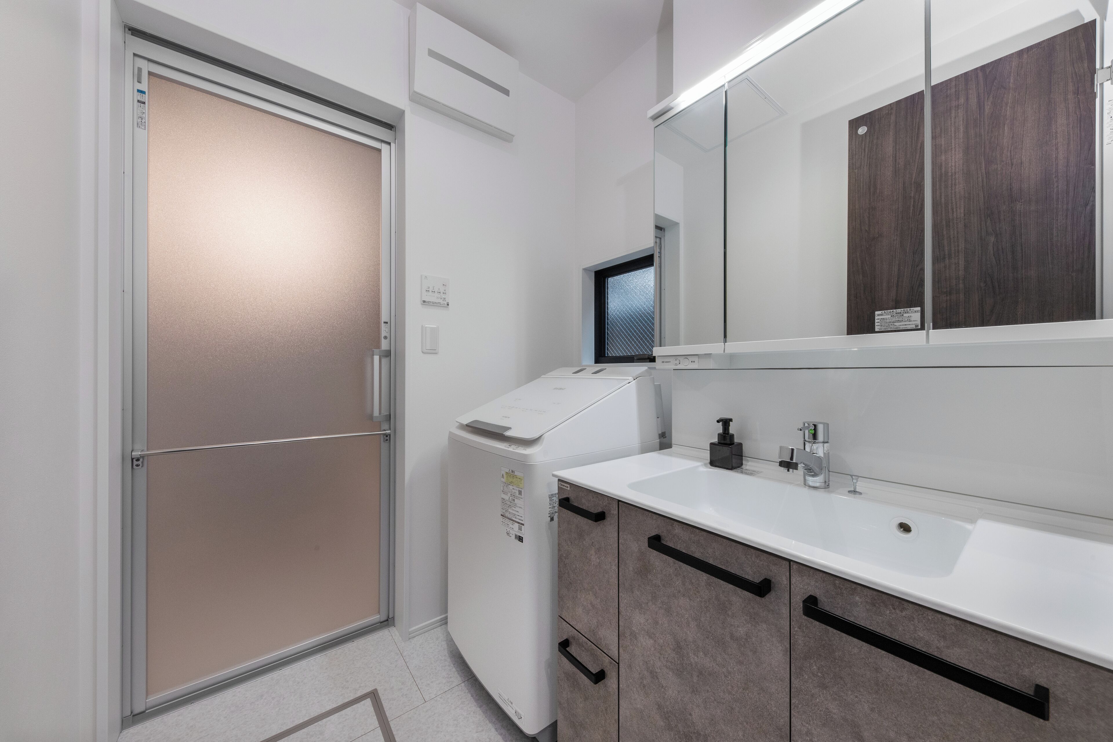 Une salle de bain moderne avec un lavabo blanc, des meubles en bois foncé, un miroir et une porte en verre dépoli.