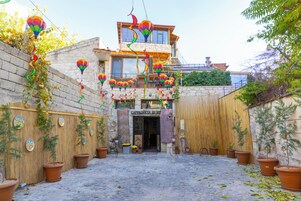 Un patio con muro de piedra, plantas en macetas y la entrada de un edificio con el letrero "Cappadocia Home".