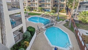 A multi-story hotel with a pool area, outdoor seating, and a view of the surrounding buildings. - Cozy Beach Retreat Close to Beach w/Courtyard Pool, Kiddie Pool, Jacuzzi & Grills! (South Padre Island)