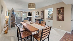 A dining area with a wooden table and chairs, a woven pendant light, and a kitchen visible through an open door. - Cozy Beach Retreat Close to Beach w/Courtyard Pool, Kiddie Pool, Jacuzzi & Grills! (South Padre Island)