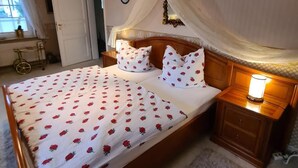 Une chambre à coucher avec un grand lit, une tête de lit en bois, des tables de chevet avec des lampes, une fenêtre avec des rideaux et un miroir sur le mur.