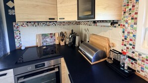Et moderne køkken med træskabe, en sort bordplade, en stålfarvet toaster og en farverig flisebaggrund.