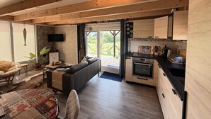 Et moderne bjælkehytteinteriør med opholdsområde, køkken og store skydedøre til en terrasse.