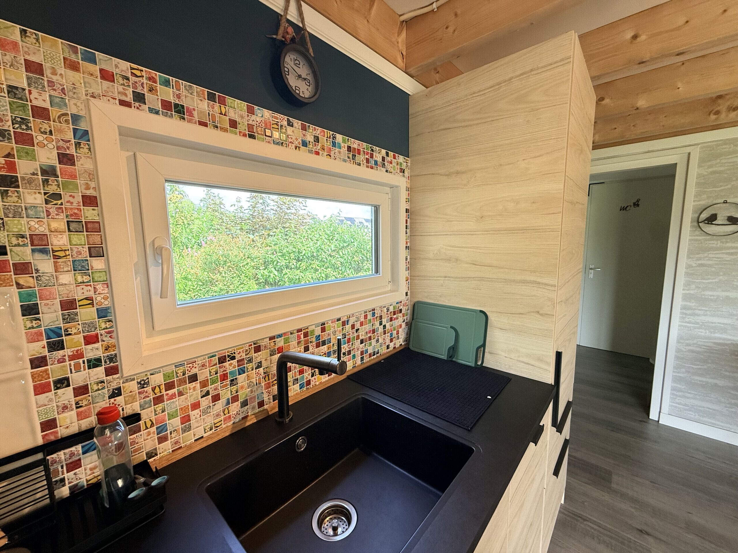 Eine moderne Küche mit farbenfroher Mosaik-Spritzschutz, einem Fenster und einem Spülbecken.