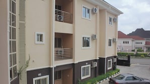 A multi-story residential building with balconies, air conditioning units, and a paved driveway with a parked car.
