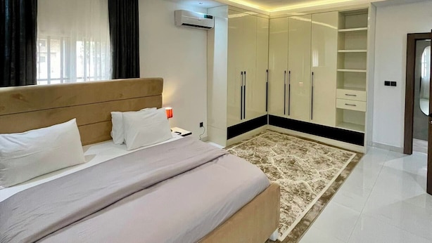 A modern bedroom with a large bed, a walk-in closet, and an air conditioning unit.