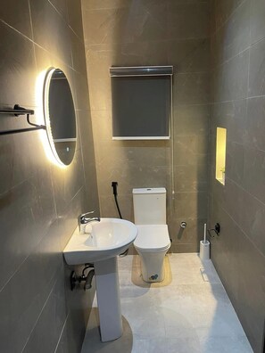 A modern bathroom with a pedestal sink, a toilet, and a wall-mounted mirror with integrated lighting.