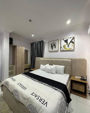 A modern hotel room with a large bed, a wardrobe, a nightstand, and two abstract paintings on the wall.
