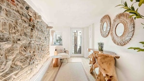 Un pasillo con pared de piedra, una mesa de madera, un sofá y dos espejos colgados en la pared.