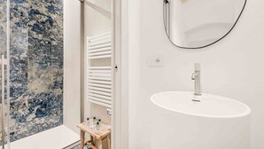 Un baño con lavamanos blanco, un espejo y cabina de ducha de vidrio.