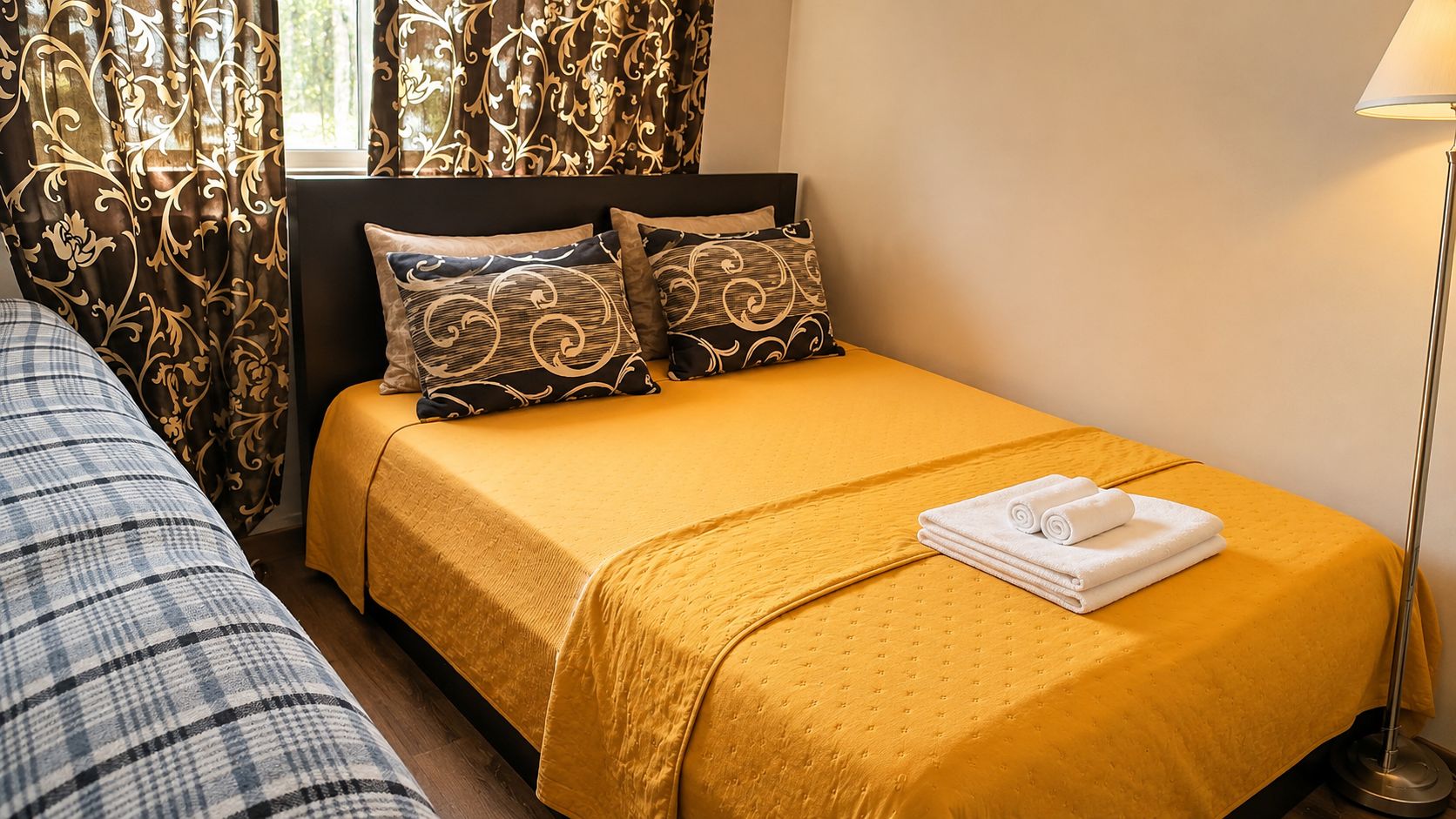 A hotel room with a single bed, a nightstand, a lamp, and a window with curtains.