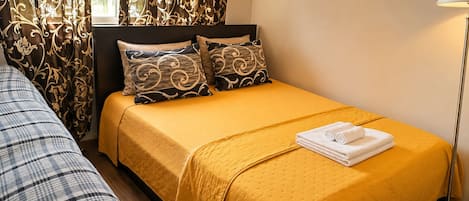 Habitación de hotel con una cama individual, una mesita de noche, una lámpara y un ventanal con cortinas.