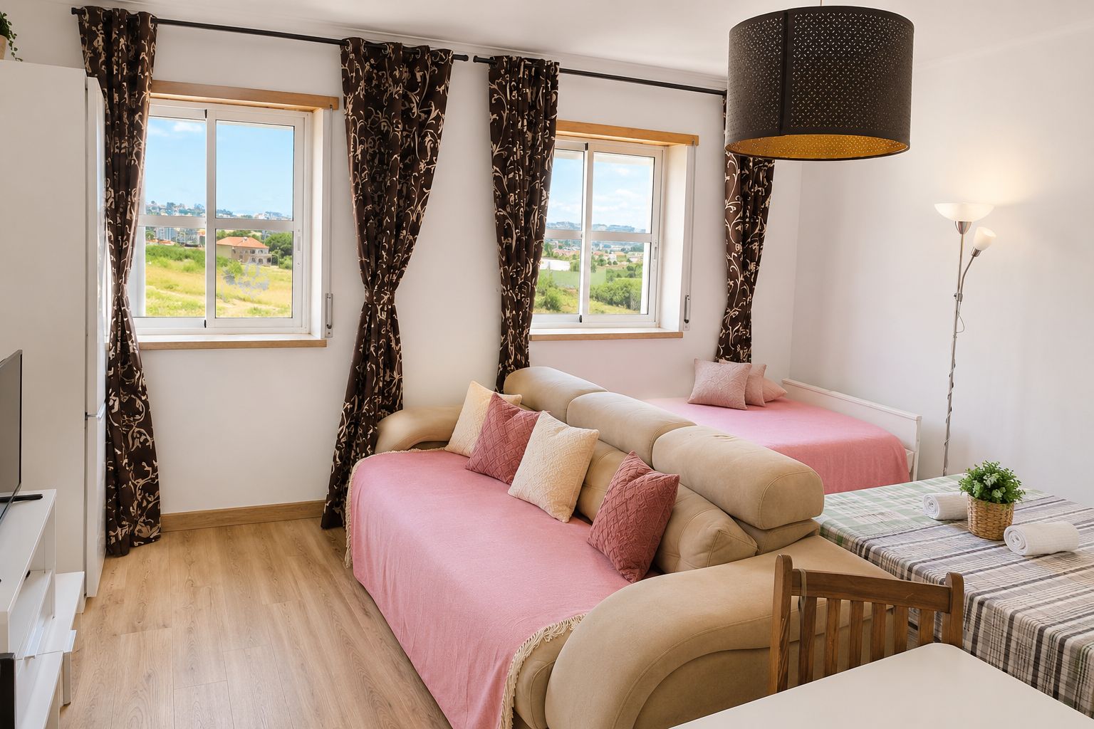 A bedroom with two beds, a table, a lamp, and a view of the outdoors.