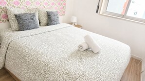 Cama bem arrumada com colcha estampada, travesseiros e toalha enrolada.