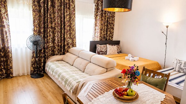 A cozy room with a sofa, a bed with a headboard, a dining table with a fruit bowl, and curtains. - Bright&spacious Apartment in Sleeps 8 Family& (Lisbon)