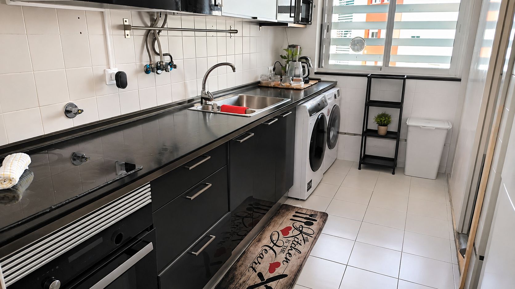 Cozinha compacta com máquina de lavar, pia e janela com vista para edifícios.