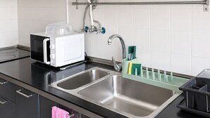 Cozinha moderna com micro-ondas embutido, pia de aço inoxidável e painel de vidro.