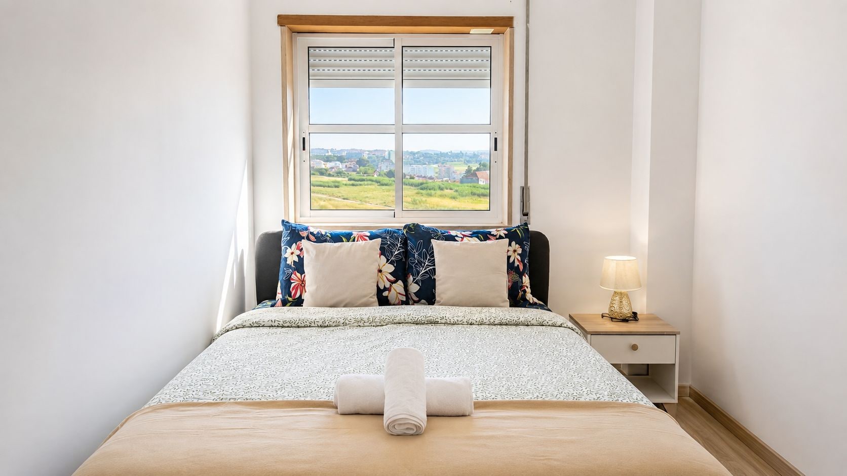 A bedroom with a bed, a nightstand, a lamp, and a window with a view of a landscape.