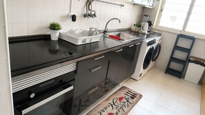 A modern kitchen with a black countertop, stainless steel appliances, a built-in washing machine, and a small potted plant. - Bright&spacious Apartment in Sleeps 8 Family& (Lisbon)