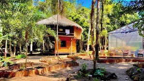 A thatched-roof structure surrounded by a garden with raised beds and a seating area with chairs. - Villa Arapiuns - 6 Bangalôs na Floresta (Santarém)