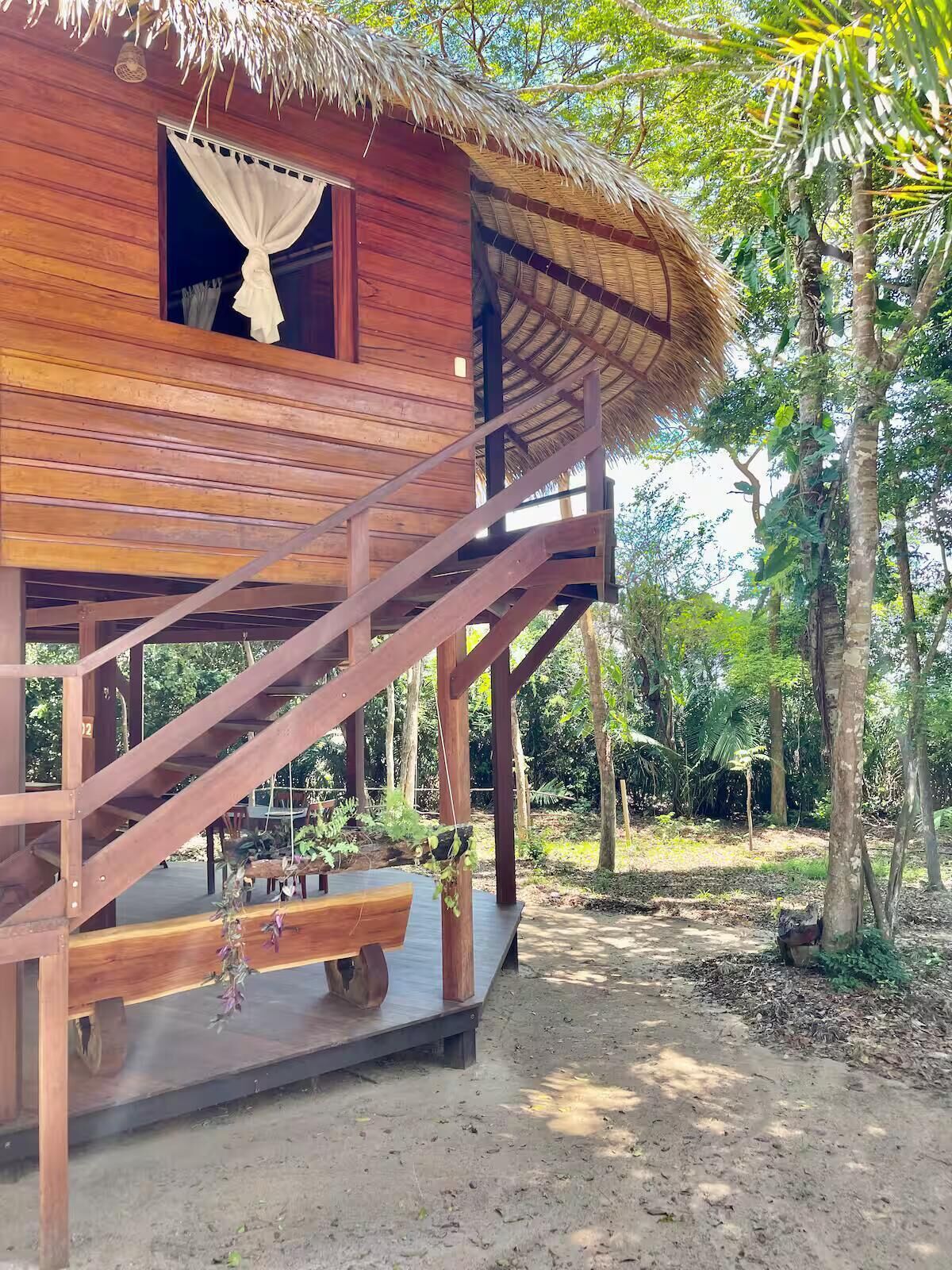 Une cabane en bois avec un toit de chaume, un escalier en bois et une terrasse en bois.