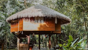 A wooden structure with a thatched roof, elevated on stilts, surrounded by dense foliage. - Villa Arapiuns - 6 Bangalôs na Floresta (Santarém)