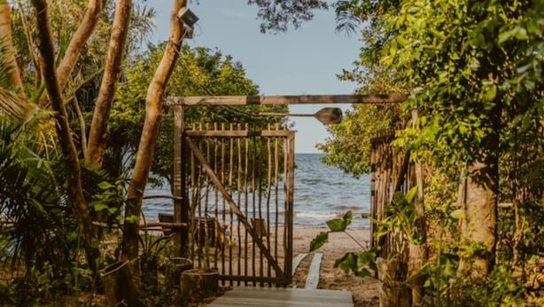 A wooden pathway leading to a beach with a rustic gate and lush greenery. - Villa Arapiuns - 6 Bangalôs na Floresta (Santarém)