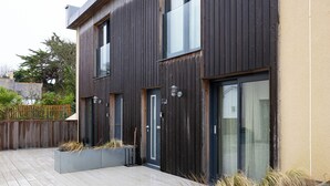 En modern tvåvåningsbyggnad med mörk träpanel, stora fönster och en träveranda med planteringslådor.