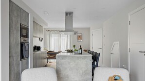 Ett modernt kök med en central köksö, inbyggda vitvaror och en matplats med en vit soffa och stolar.