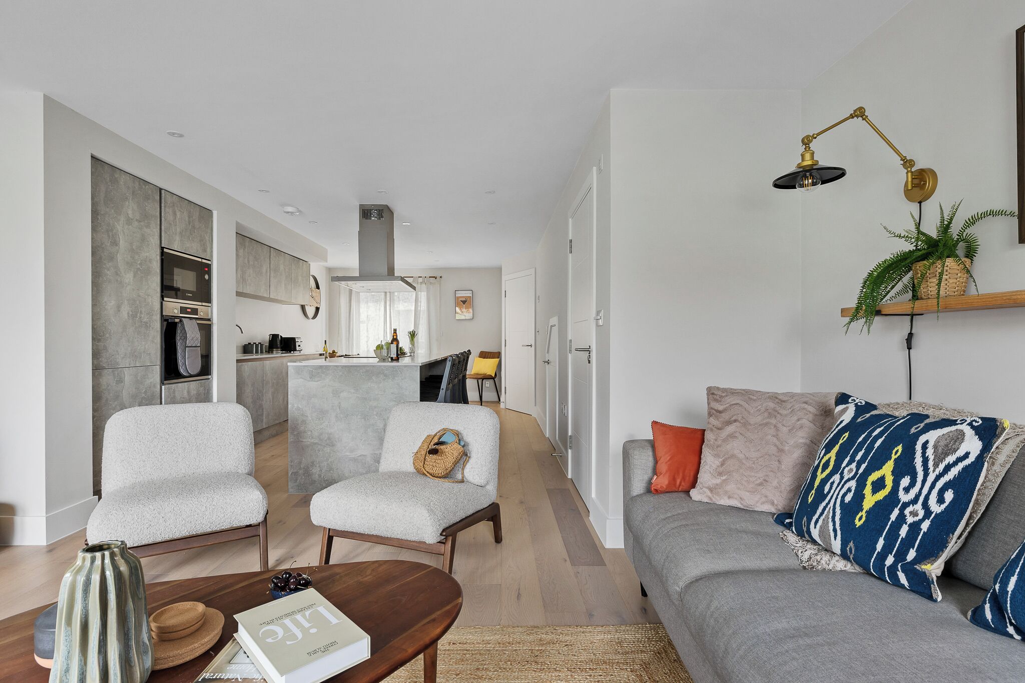 A modern living room with a grey sofa, two armchairs, a coffee table, and a bookshelf.