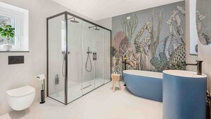 Un baño moderno con ducha de vidrio, inodoro independiente, una bañera grande y aislada, y un mural de plantas acuáticas.