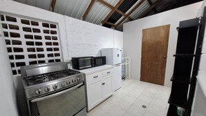 Cocina compacta con estufa a gas, horno, microondas y un armario blanco.