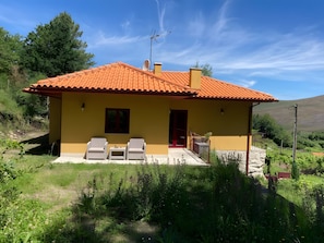 A yellow house with a red-tiled roof, two white chairs, and a small table outside. - Casa dos Mirtilos, Germil – Mountain Retreat in Gerês (Germil)