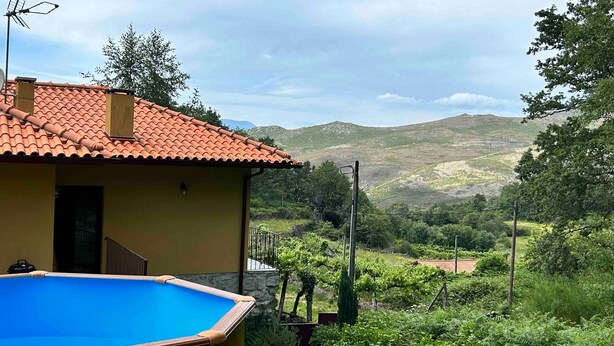 Uma casa com piscina, telhado de telhas vermelhas e vista para uma paisagem montanhosa.