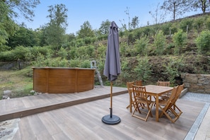 An outdoor seating area with a wooden table and chairs, a wooden hot tub, and a covered umbrella. - Casa dos Mirtilos, Germil – Mountain Retreat in Gerês (Germil)