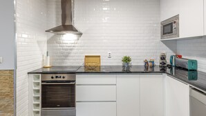 Cozinha compacta com azulejos brancos tipo metrô, coifa de aço inoxidável, forno embutido e micro-ondas sobre a bancada.