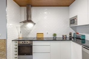 A compact kitchen with white subway tiles, a stainless steel range hood, a built-in oven, and a microwave above the counter. - Casa dos Mirtilos, Germil – Mountain Retreat in Gerês (Germil)