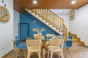 Uma área de jantar com mesa de vidro, cadeiras de madeira e parede azul.
