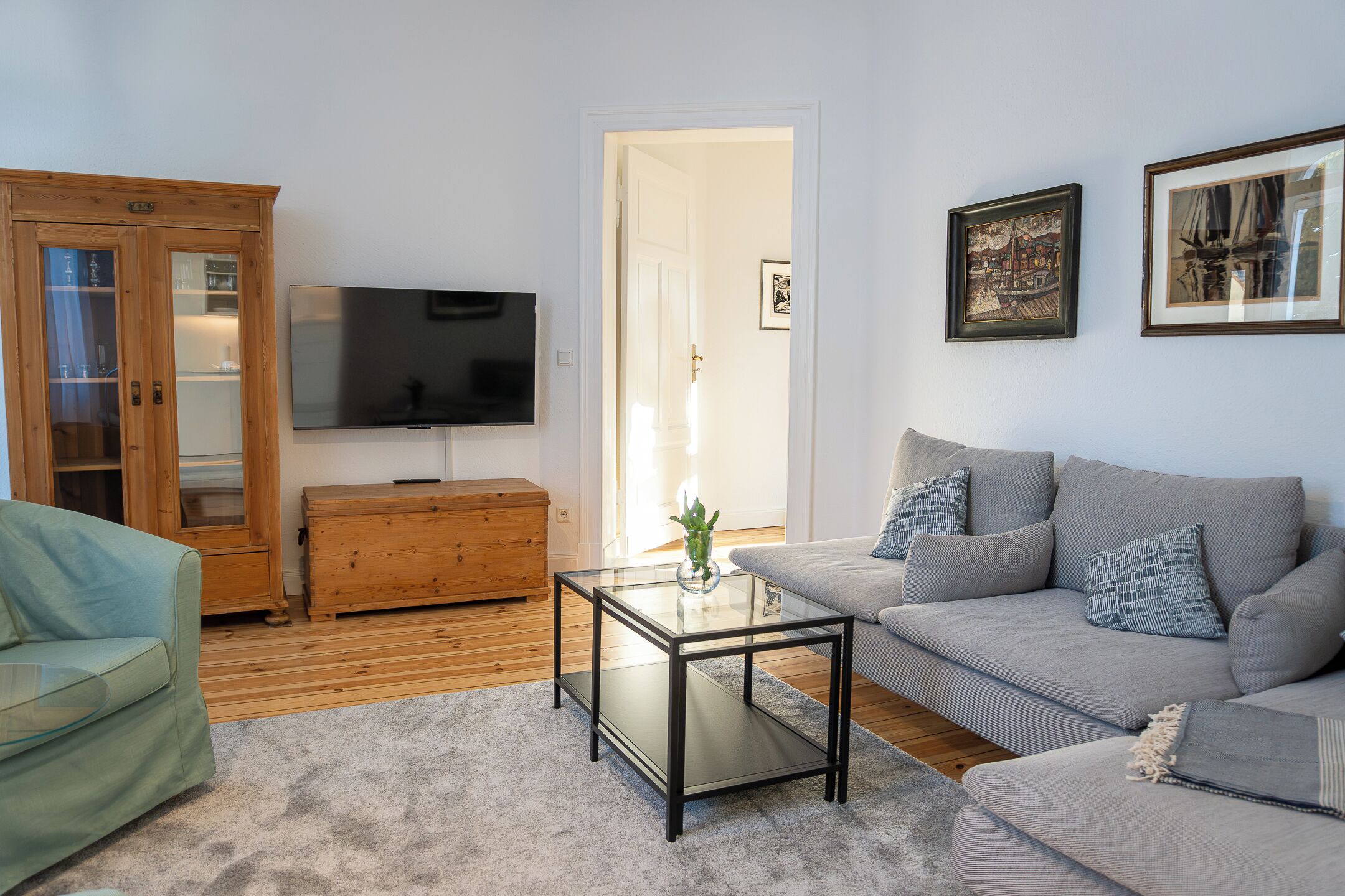 A living room with a sofa, a glass coffee table, a wooden cabinet, and a television.