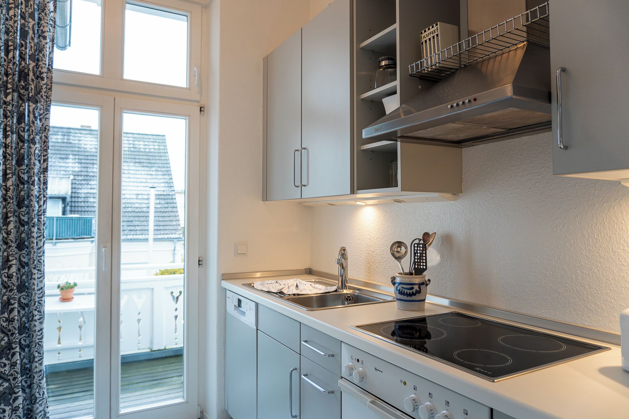 Une cuisine moderne avec des meubles blancs, un évier en acier inoxydable et une cuisinière électrique.