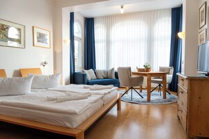Una habitación de hotel con una cama grande, un sofá, una mesa de comedor con sillas, un televisor y un aparador.